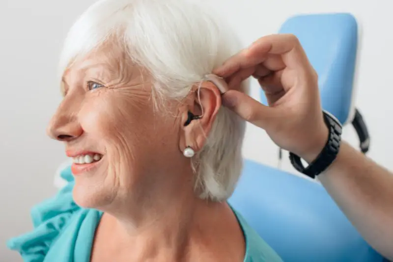 Audiologist showing a woman how to put in hearing aids